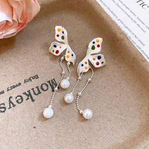 Dettaglio di orecchini a farfalla smaltati con pois colorati e nappe di perle
