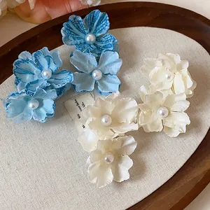 Detail shot of elegant fabric flower hair clips with pearl centers on a rustic wooden tray
