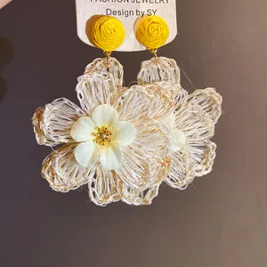 Close-up of handmade raffia flower pendant earrings with yellow stud detail