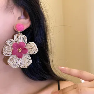 Close-up detail of stylish woven raffia flower drop earrings with magenta accents