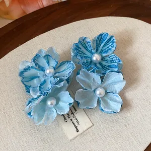 Detail showing elegant blue fabric flower hair clips with central pearl accents.