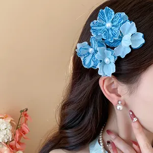 Detail of blue fabric flower hair clip with pearl center on brunette hair.