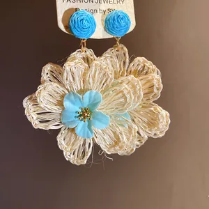 Detailed macro view of woven raffia flower drop earrings with blue floral center