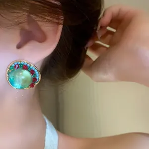 Close-up of vintage geometric earring with large green stone and colorful rhinestones