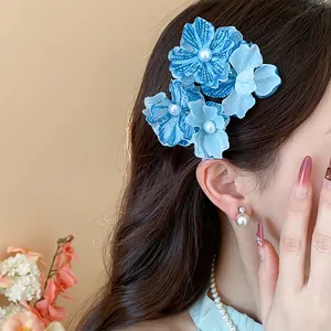 Close-up view of elegant blue fabric flower hair clip with pearl details worn by a model