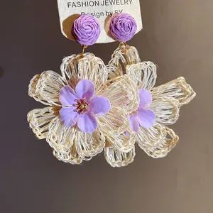 Detailed view of handmade raffia flower drop earrings with purple fabric petals