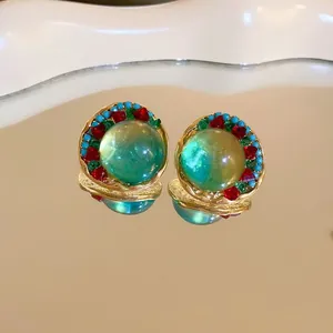 Close-up of vintage-style geometric earrings with green orb and colorful crystals.