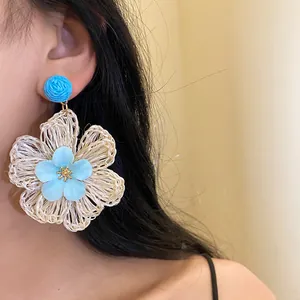 Detailed view of a handmade woven raffia flower drop earring on a female model