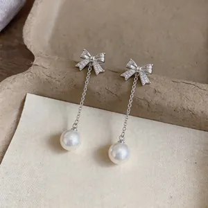 Detailed macro shot of silver bow earrings with zircon stones and elegant white pearl drops.