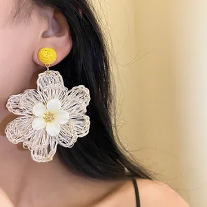 Detailed close-up view of handmade cream raffia flower drop earring worn on model ear