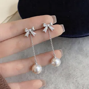 Close-up of elegant bow stud earrings with long pearl tassels and shimmering zircons