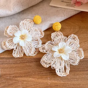 Close-up of woven raffia flower drop earrings with white fabric center and yellow stud.