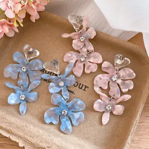 Close-up of floral acetate drop earrings with heart studs and sparkling rhinestones.