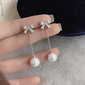 Detail of elegant silver bow earrings with zircon and dangling white pearls