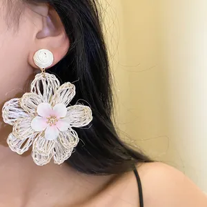 Close-up detail of a large hand-woven raffia flower drop earring worn by a model