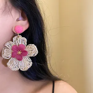 Close-up detail of large pink and white woven raffia flower earrings worn by a model