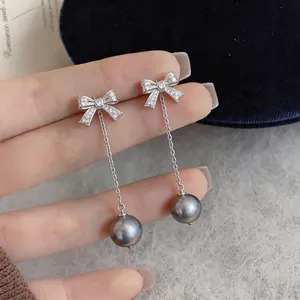 Detailed view of silver bow earrings with zircon stones and dangling grey pearl.