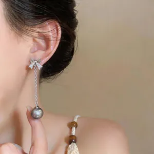 Detail of silver bow-knot stud earring with tassel and dark grey pearl on ear.
