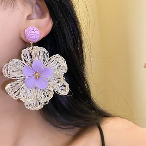 Detailed view of a purple and beige raffia flower pendant earring worn by a model