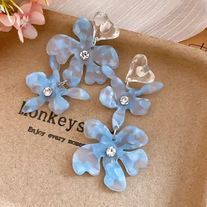 Close-up of light blue marbled acetate flower earrings with clear heart-shaped studs