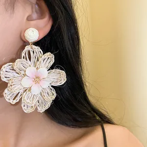 Close-up of elegant handmade white raffia flower drop earrings worn by a model