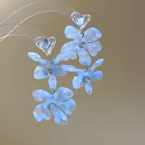 Detailed macro view of blue acetate flower earrings with sparkling rhinestone centers and heart studs