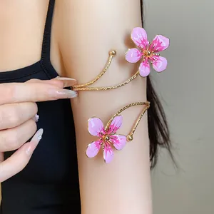 Close-up of elegant gold arm cuff featuring two pink enamel flowers on woman's arm