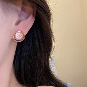 Primer plano de un elegante pendiente redondo de resina en oro rosa colocado en la oreja