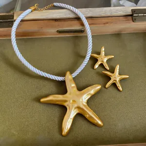 Vue détaillée du collier pendentif étoile de mer dorée avec corde blanche et boucles d'oreilles.
