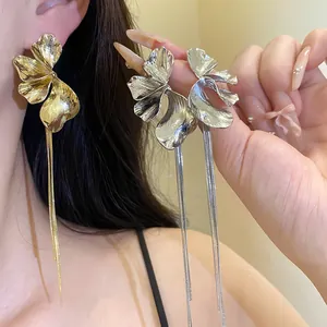Detailed view of elegant gold and silver flower tassel earrings being worn and held.