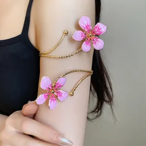 Detailed view of a gold metal arm cuff featuring pink enamel flowers on a model's arm.