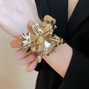 Macro view of oversized metallic gold flower bangle bracelet worn on wrist with a black blazer