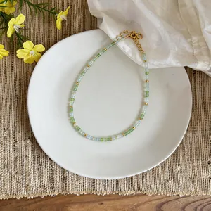 Close-up detail of a delicate green glass bead necklace displayed on a white ceramic plate