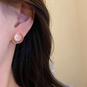 Elegantes pendientes redondos de oro rosa con incrustación perlada puestos en la oreja