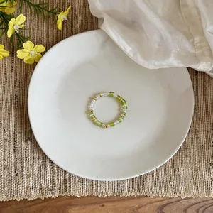 Elegant handmade green and gold glass beaded ring shown on a white ceramic plate