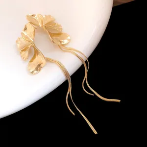 Detailed macro view of gold flower earrings with long tassel chains on a white plate
