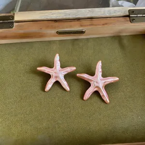 Gros plan d'un bijou étoile de mer en émail nacré rose sur un fond vert texturé