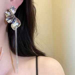 Close-up of silver flower stud earrings with long metal tassels worn on model's ear