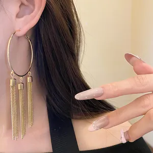 Close-up of a large gold hoop earring with elegant triple chain tassels on model