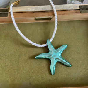 Gros plan d'un pendentif étoile de mer turquoise sur un collier en cordelette blanche.