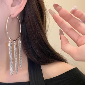 Detailed view of large silver hoop earrings featuring triple hanging chain tassels on a model.
