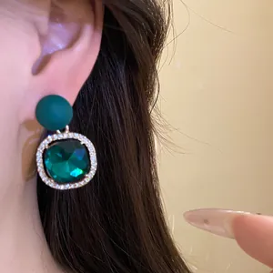 Close-up detail of a dark green matte stud earring with a square green gem drop