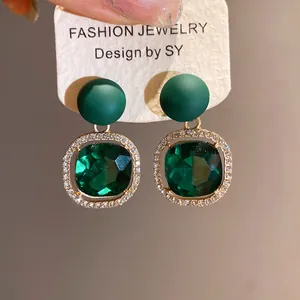 Detailed macro view of emerald green square gem earrings with rhinestone border.