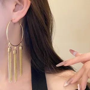 Close-up detail of golden hoop earring featuring triple dangling tassel chains on model