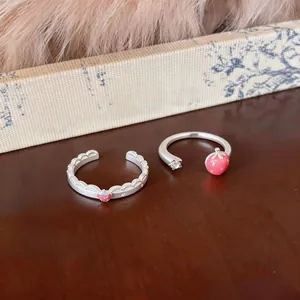Primo piano di due anelli aperti color argento con ciondoli a fragola rosa su tavolo.