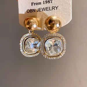 Close-up detail of gold-finish earrings featuring large clear square crystals.