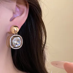 Macro shot of a luxury gold drop earring with a faceted central crystal worn on the ear.