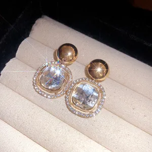 Detailed macro view of square crystal earrings with rhinestone halo in gold finish