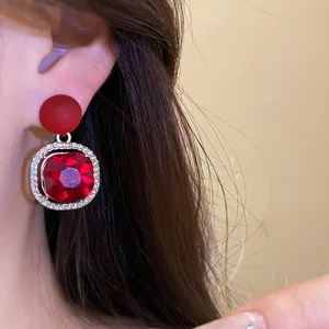 Close-up of elegant red gemstone earrings with rhinestone frame detail on an ear model.