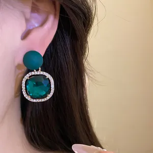 Close-up of emerald green crystal stud earrings with rhinestone halo on model's ear